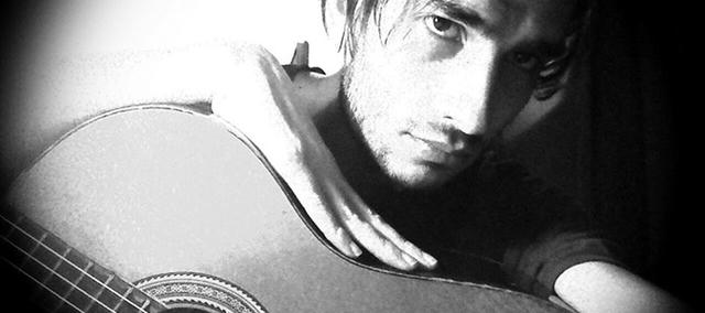 L'immagine bianca e nera di un uomo che suona una chitarra, con una cinghia Fender visibile, che guarda giù e si tocca il viso, con il logo della band "RADIOHEAD" stampato sulla sua maglietta.